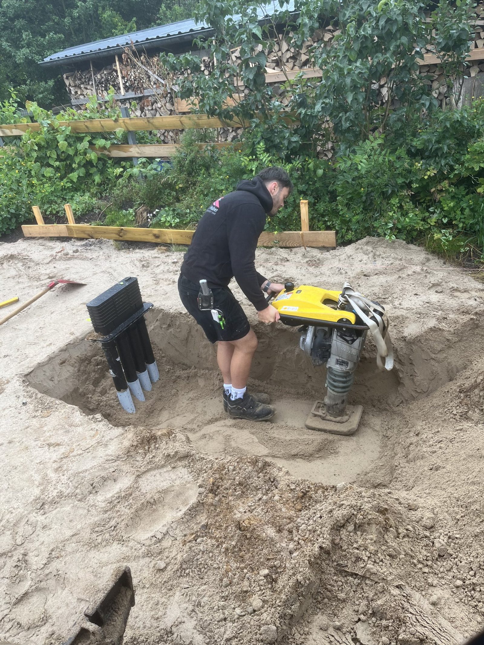Verdichten des Sandbetts mit der Rüttelplatte, daneben das Entwässerungsrohr